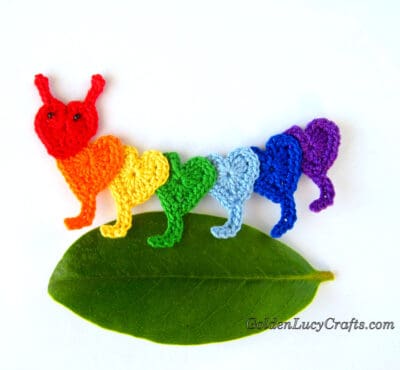 Crocheted rainbow caterpillar on a green leaf. 