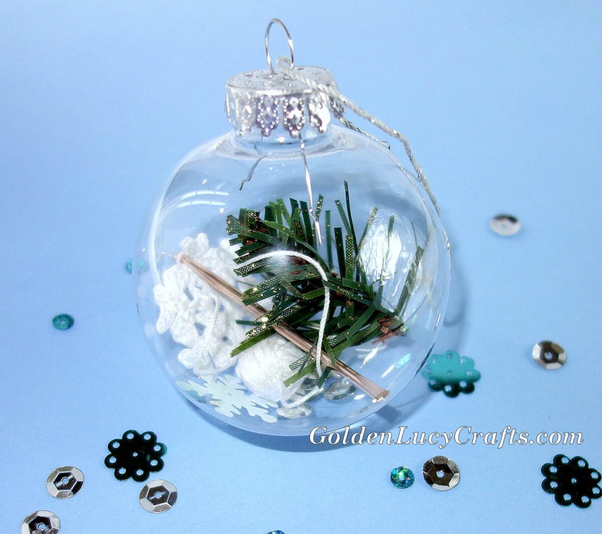 Handmade clear ball Christmas ornament filled with piece of Christmas tree, small crochet snowflake and crochet hook.
