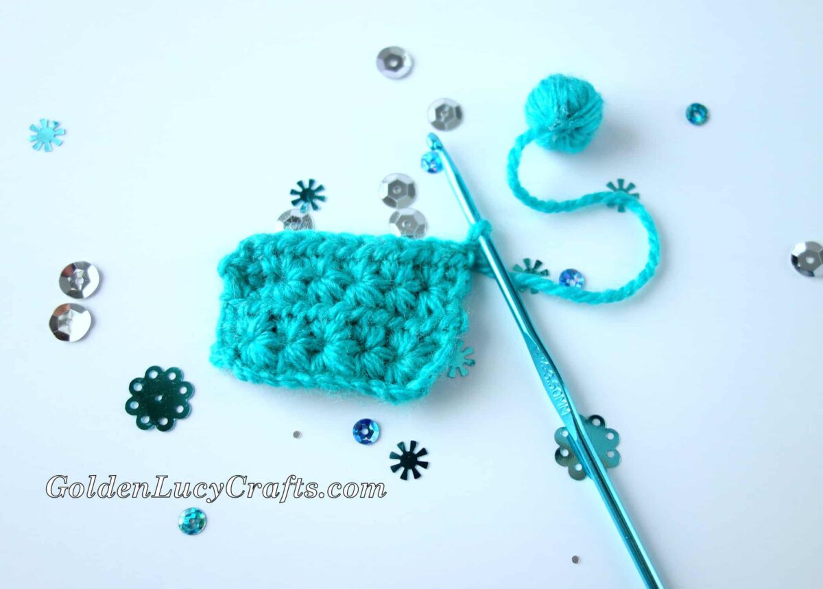 Small swatch crocheted from blue yarn, crochet hook and tiny ball of yarn.