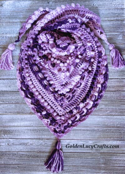 Crochet purple shawl laying on the wooden surface.
