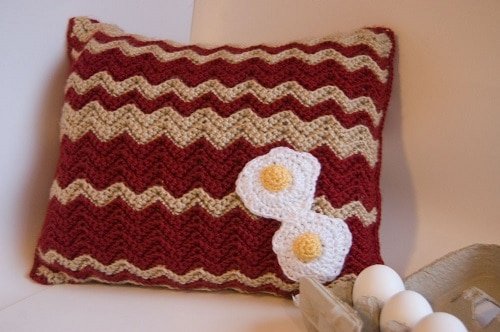 Crocheted pillow that looks like bacon and embellished with crocheted eggs.