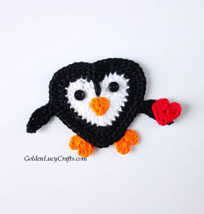 Crochet pengiun with small red heart in his flipper.