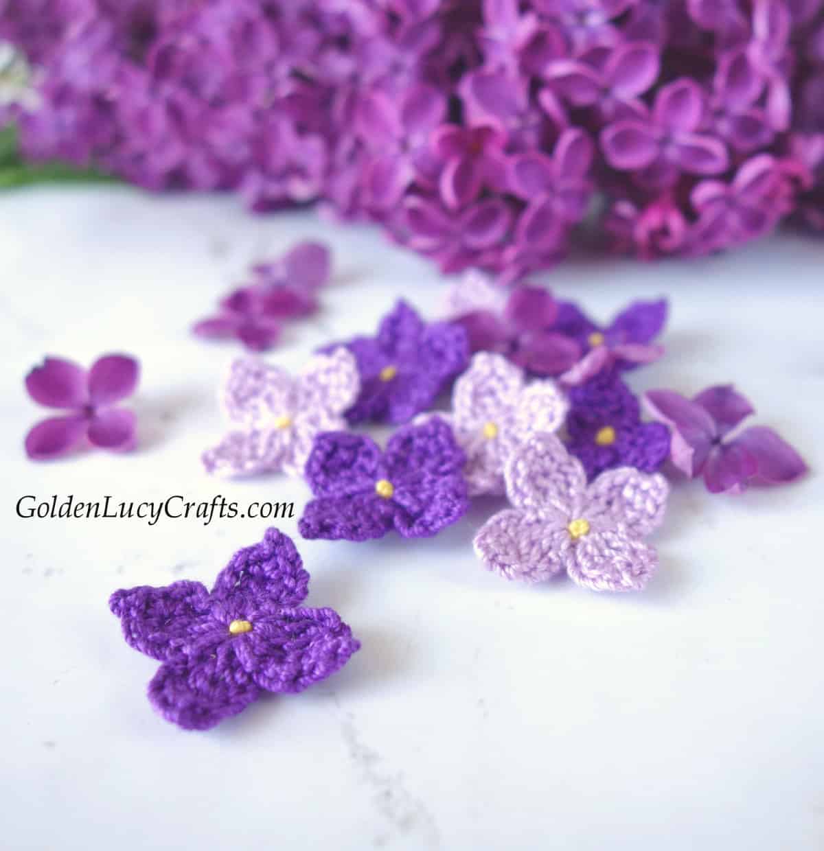 Crocheted lilac flowers, real lilac in the background.
