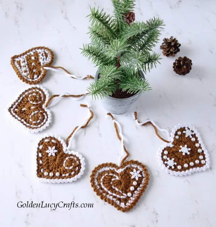 Crochet gingerbread hearts laying around small Christmas tree.