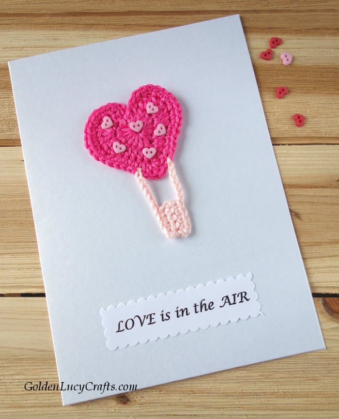White card with crochet hot heart air balloon applique and text saying love is in the air.