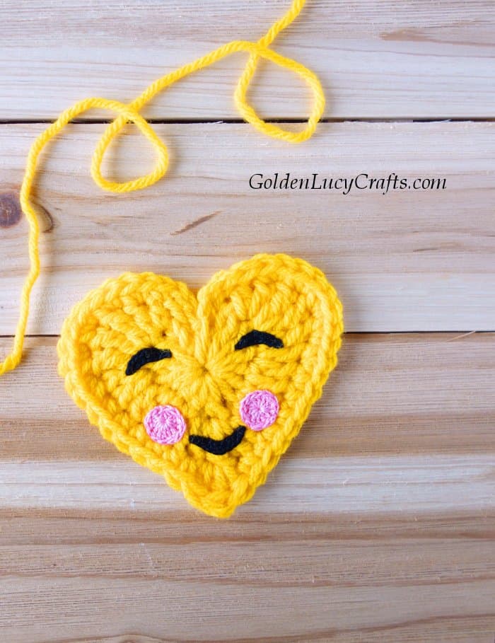 Crochet heart-shaped emoji and yellow yarn.