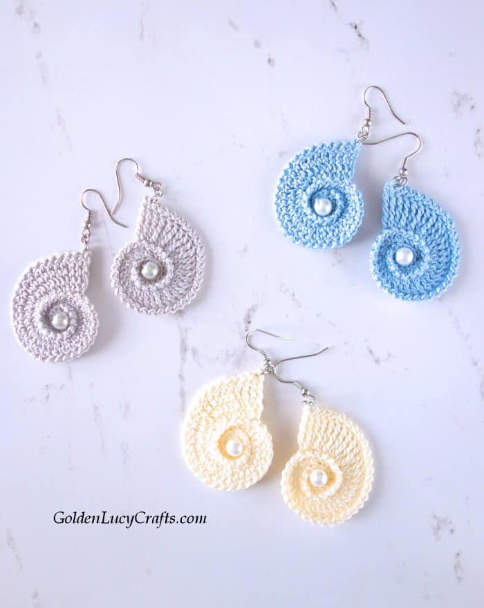 Three pairs of crochet seashell earrings in light blue, cream and grey colors.