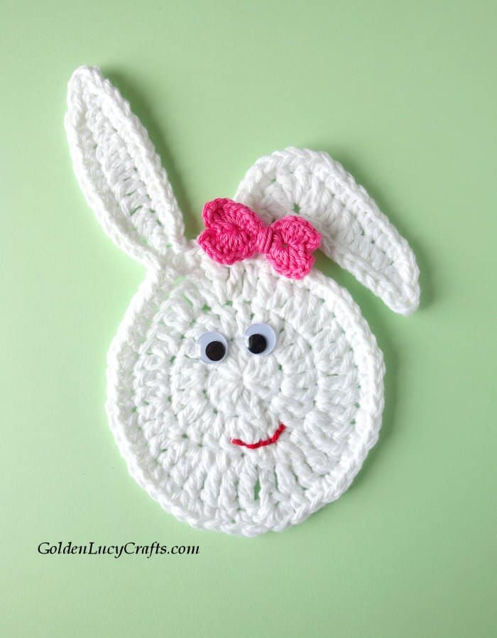 Whtie crocheted Easter bunny face with googly eyes  and small pink bow.