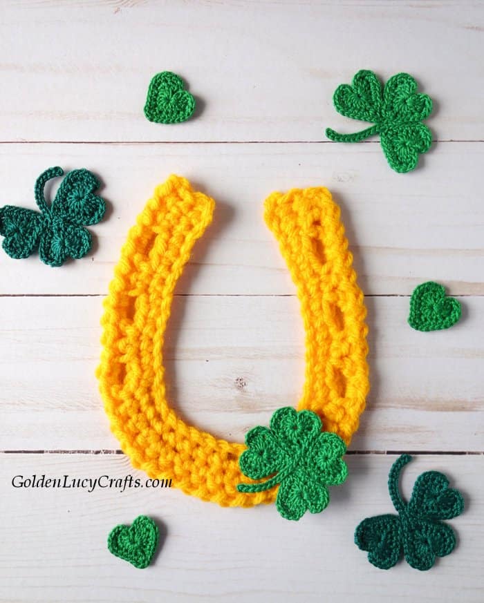Crochet yellow horseshoe applique, green shamrocks and hearts around. 