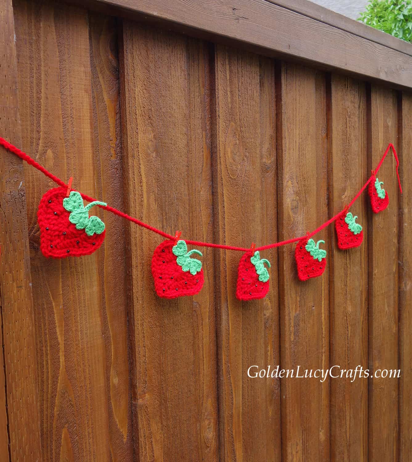 Crocheted strawberry garland hanging on the blown fence.