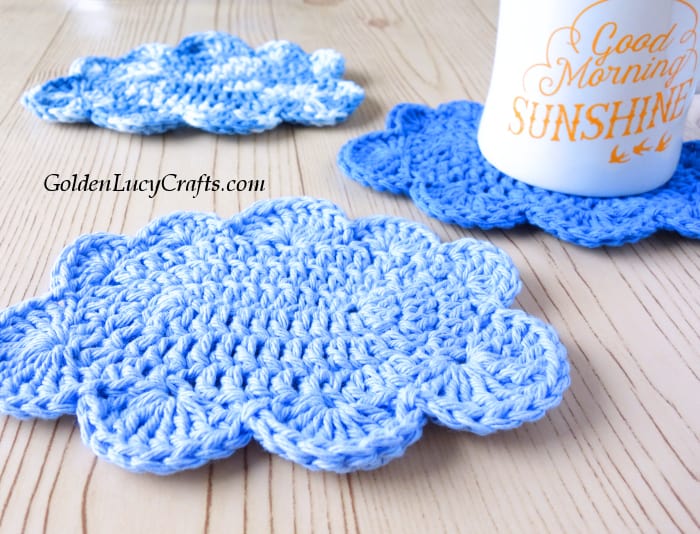 Three crocheted cloud coasters with mug on one of them.