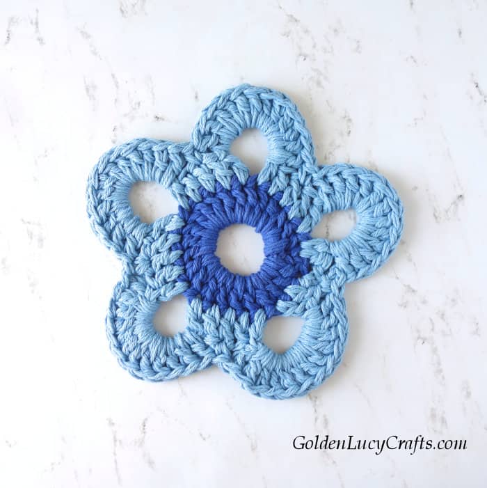 Crocheted flower with dark blue center and light blue petals.