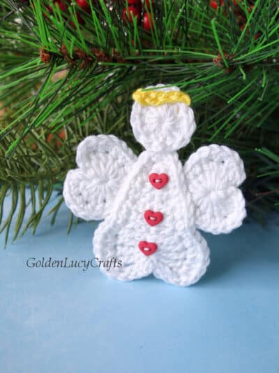 Crochet heart angel applique near the Christmas tree branch.