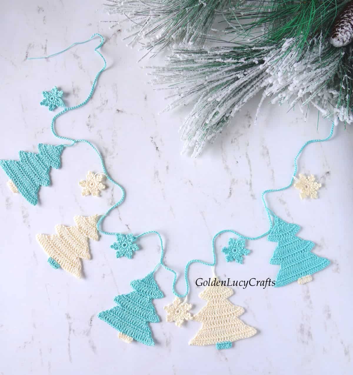 Crochet Christmas tree garland in turquoise and cream color laying flat on the table