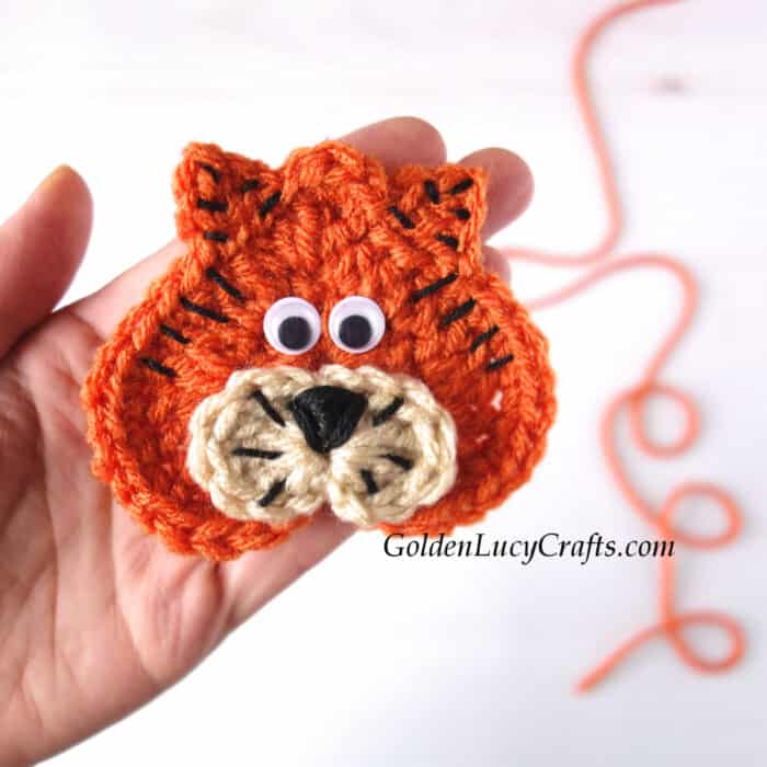 Crochet heart tiger applique in the palm of a hand.