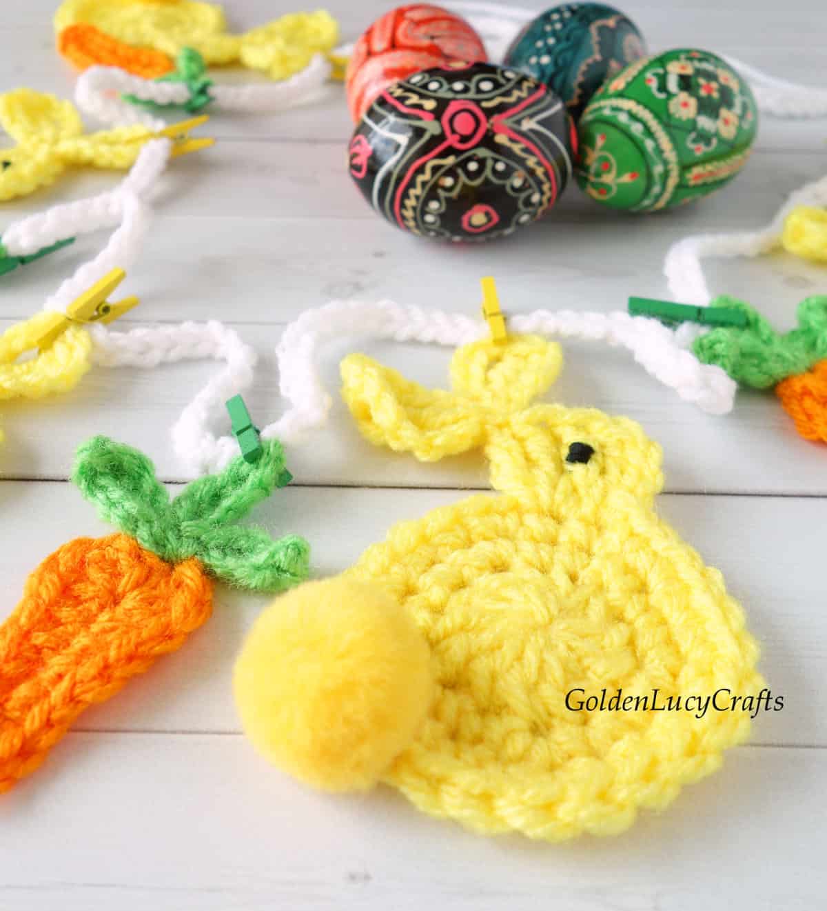 Crocheted Easter bunny garland close up picture, painted Easter eggs in the background.