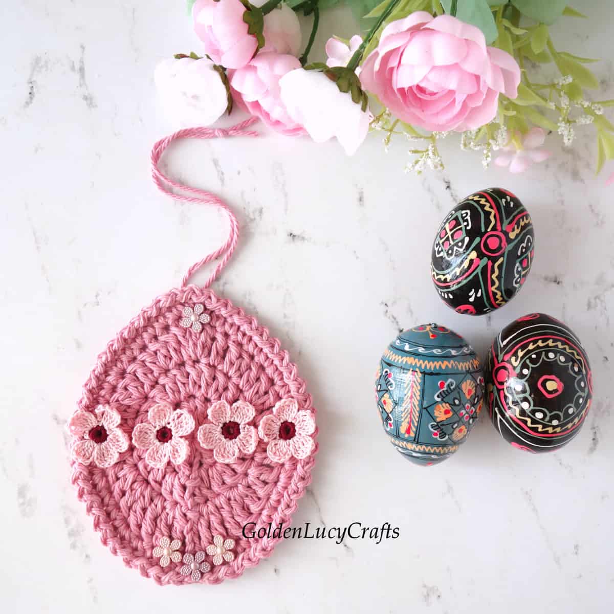 Crocheted Easter egg ornament embellished with small flowers, three wooden painted eggs next to it.