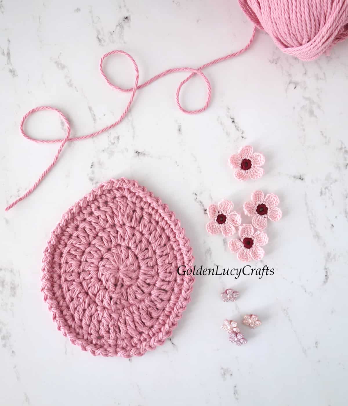 Crocheted flat egg shape, four small flowers, buttons and skein of yarn.