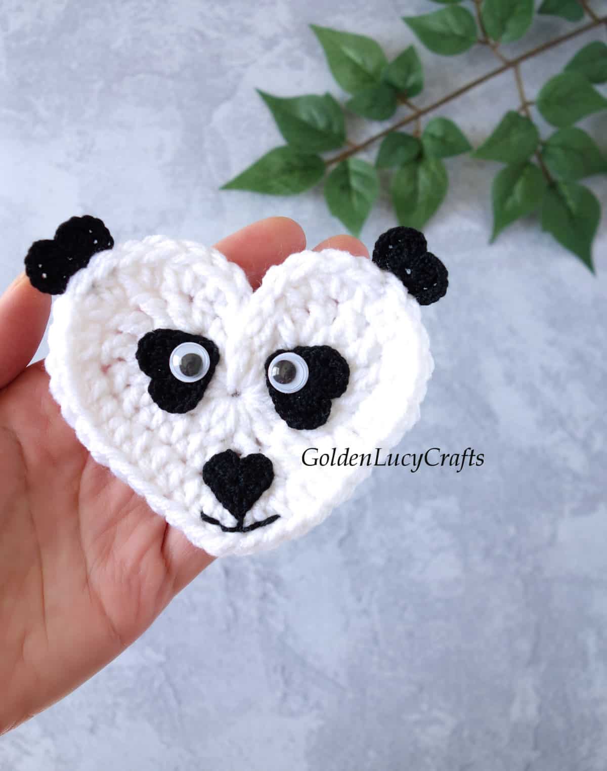 Crochet panda applique in the palm of a hand.