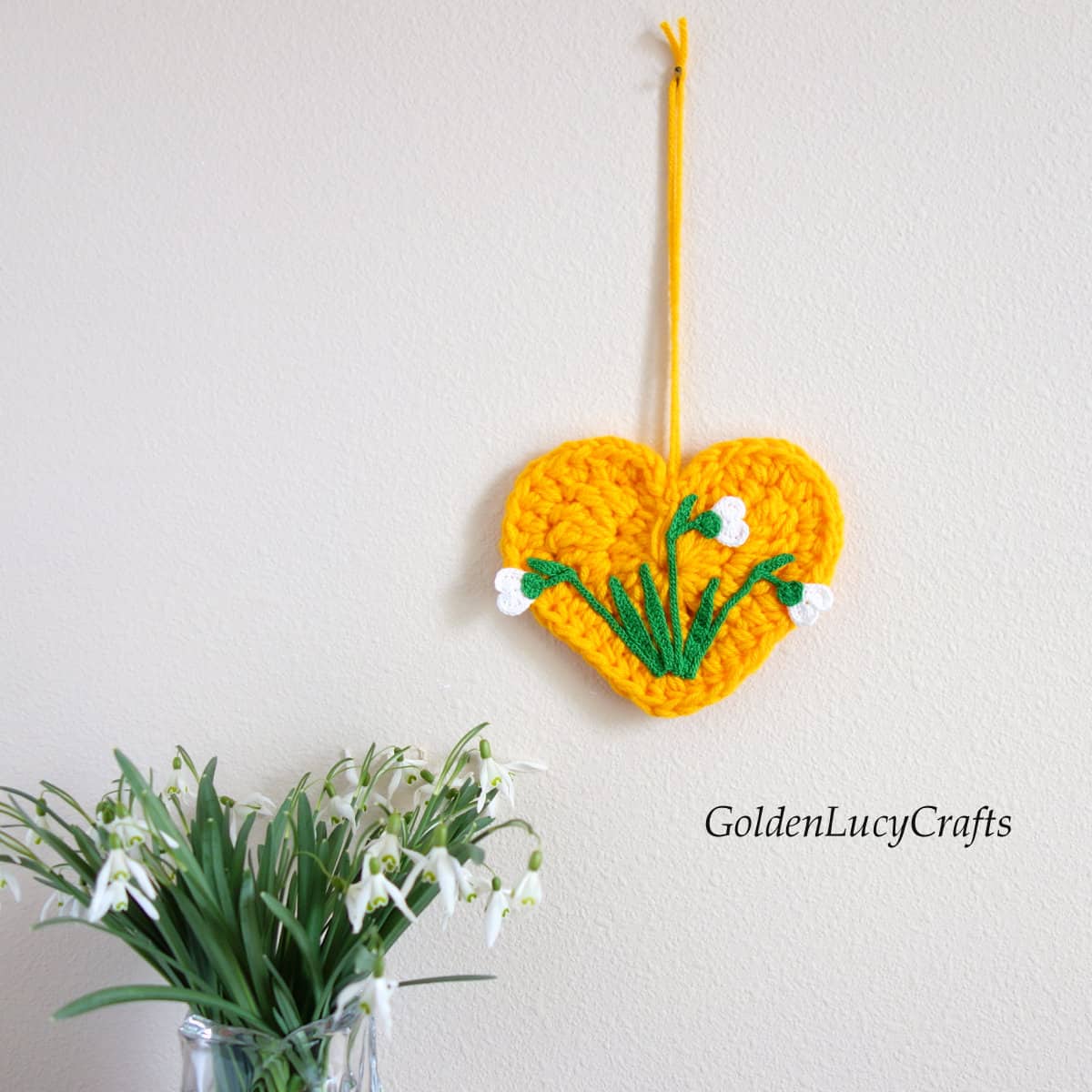 Crocheted yellow heart with crocheted snowdrops on it wall decor, real snowdrops in a vase.