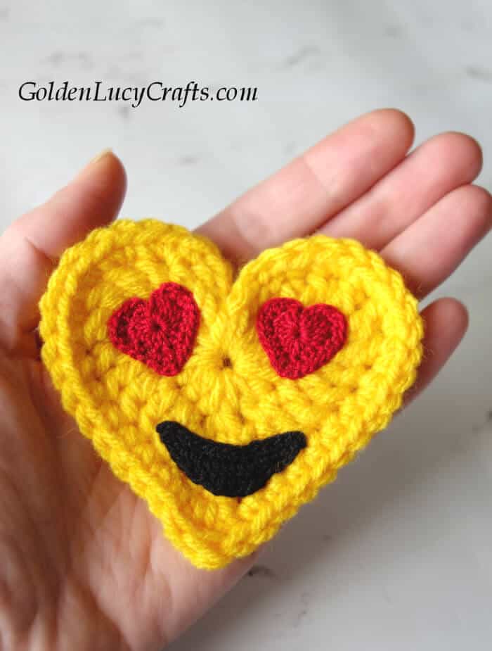 Crochet heart-eyes emoji in the palm of a hand.