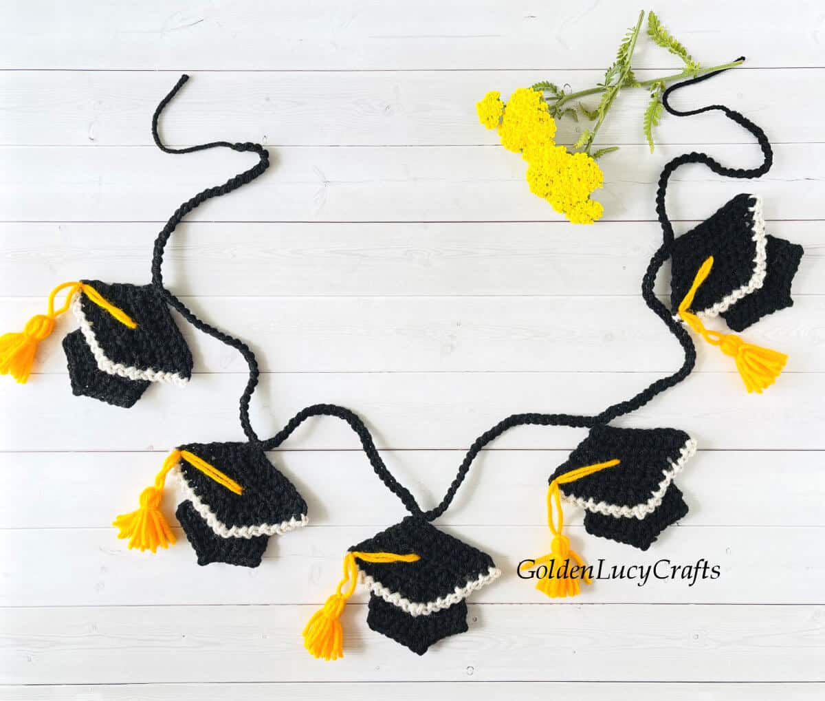 Crocheted graduation garland laying on the surface, yellow flowers in the background.