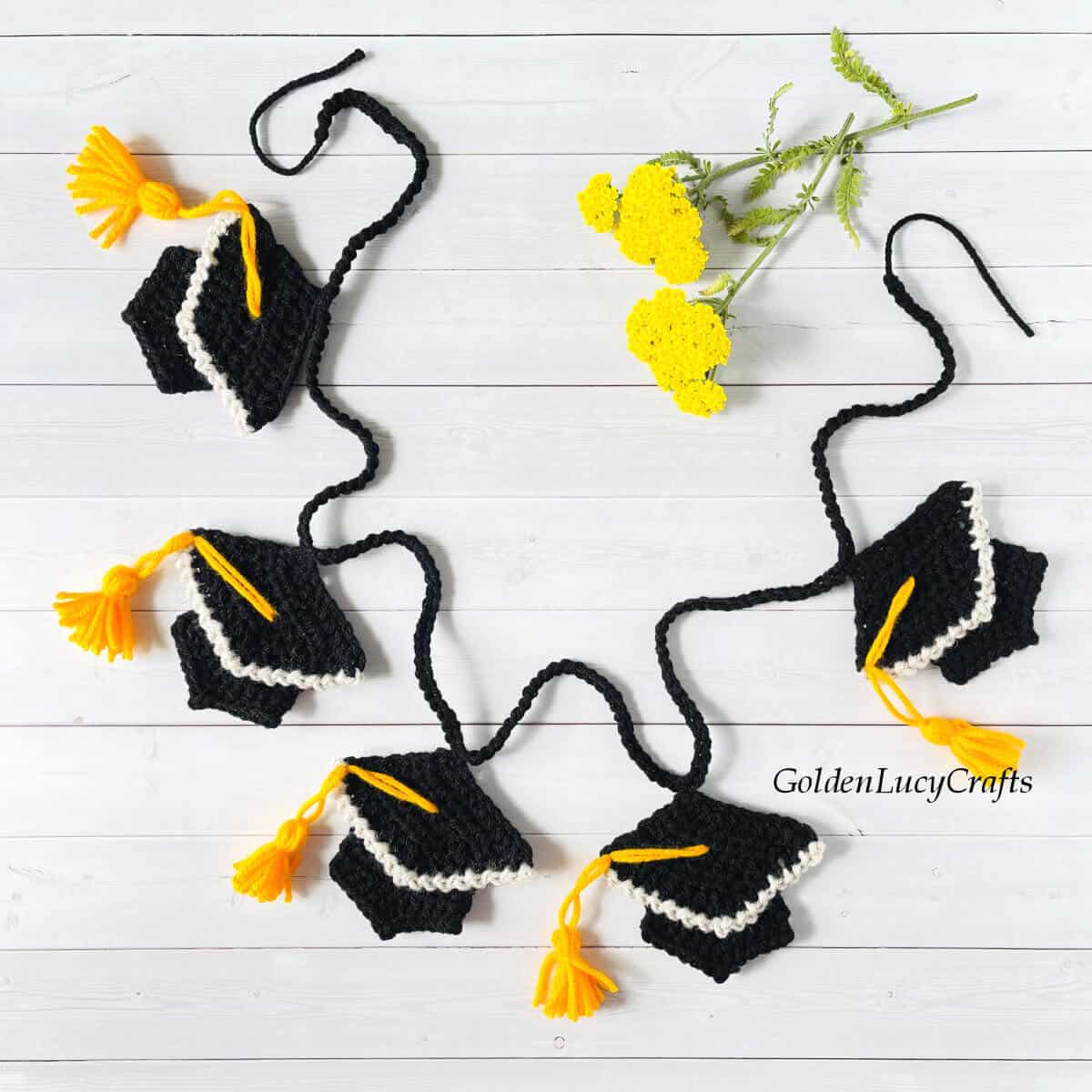 Crocheted graduation garland laying on the surface, yellow flowers in the background.