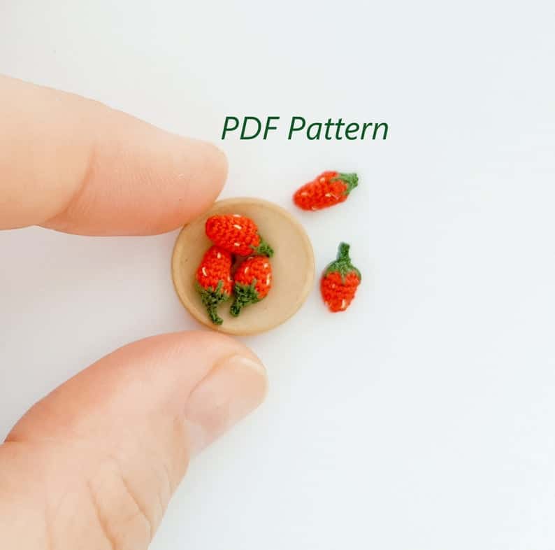 Tiny crochet strawberries held by fingertips.