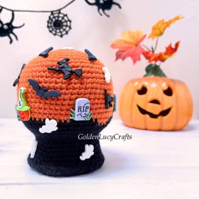 Crocheted Halloween snow globe, Jack-o'-lantern in the background.