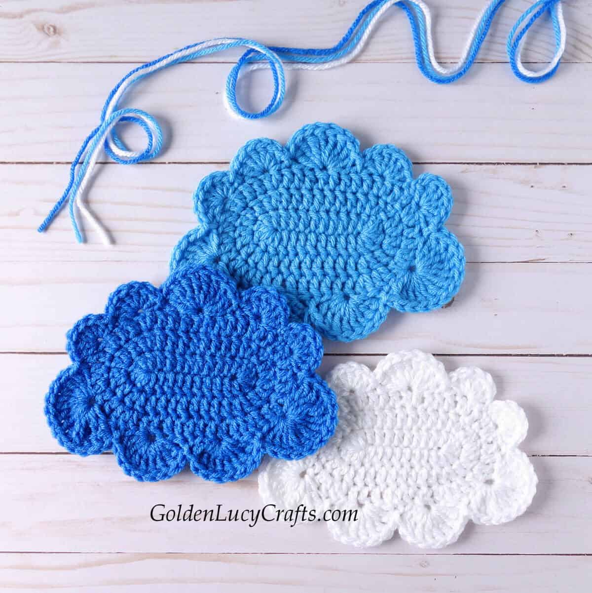 Three crocheted cloud appliques in white, blue and light blue colors.