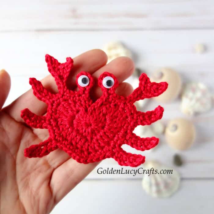 Crocheted red crab applique in the palm of a hand.