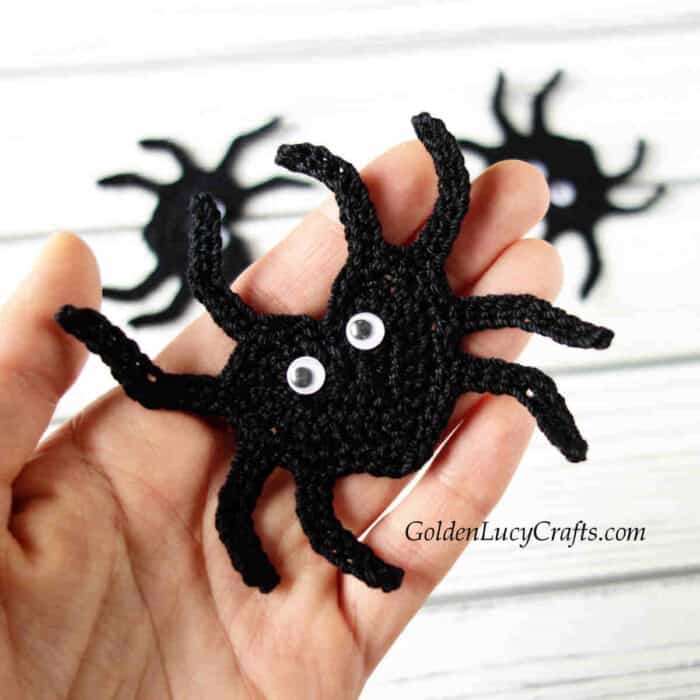 Crocheted black spider applique in the palm of a hand.