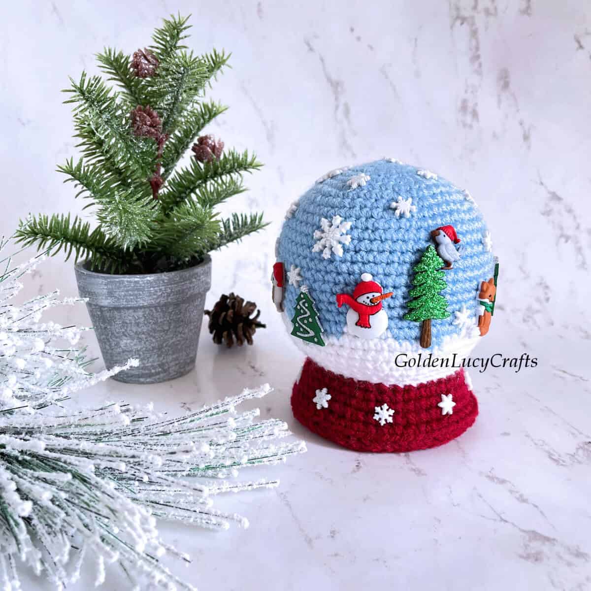 Crocheted snowglobe toy embellished with winter-themed buttons.