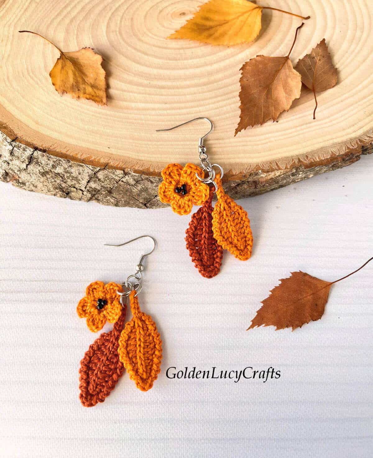 Crocheted earrings, wood slice and fall leaves in the background.