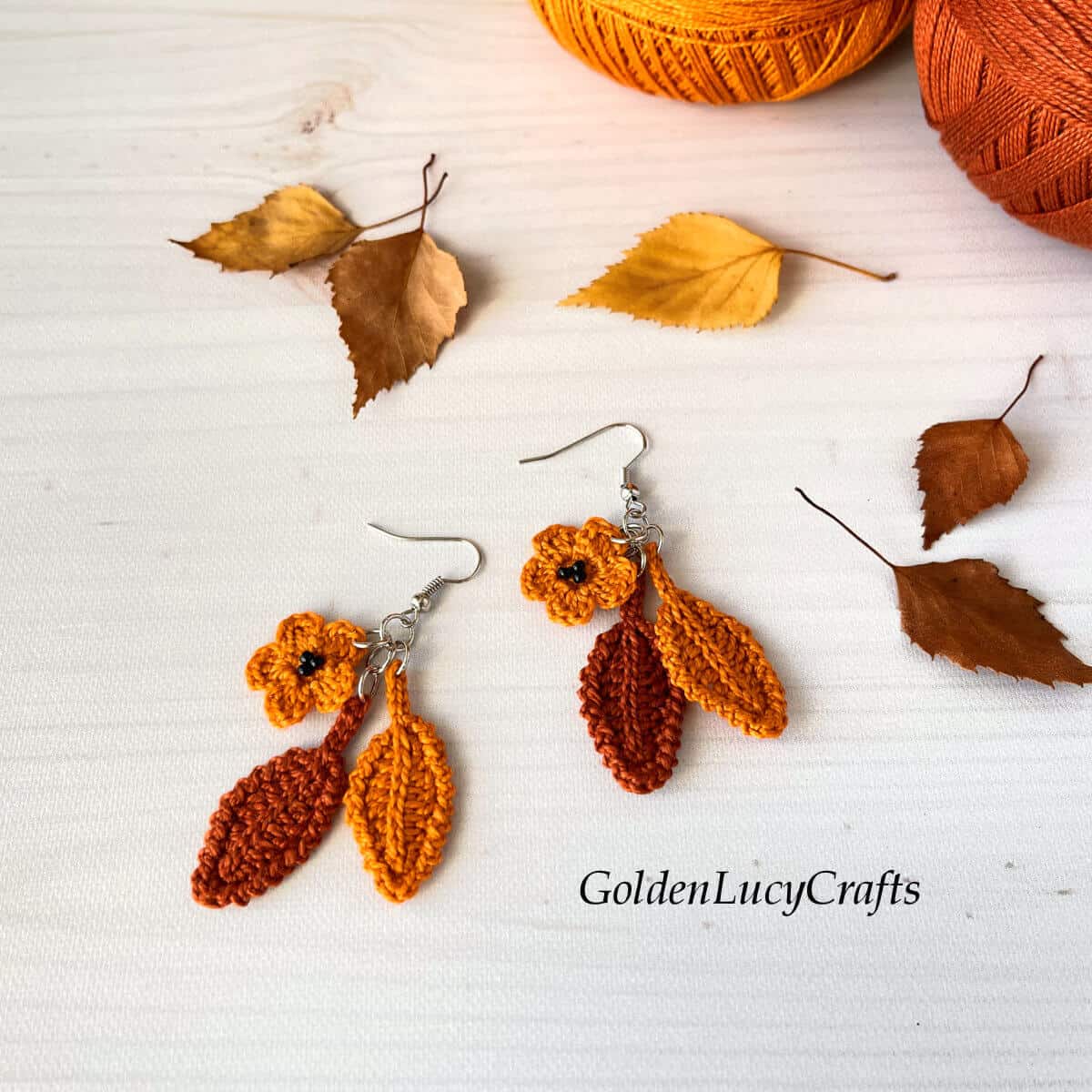 Crochet fall earrings, leaves and two balls of thread in the background.