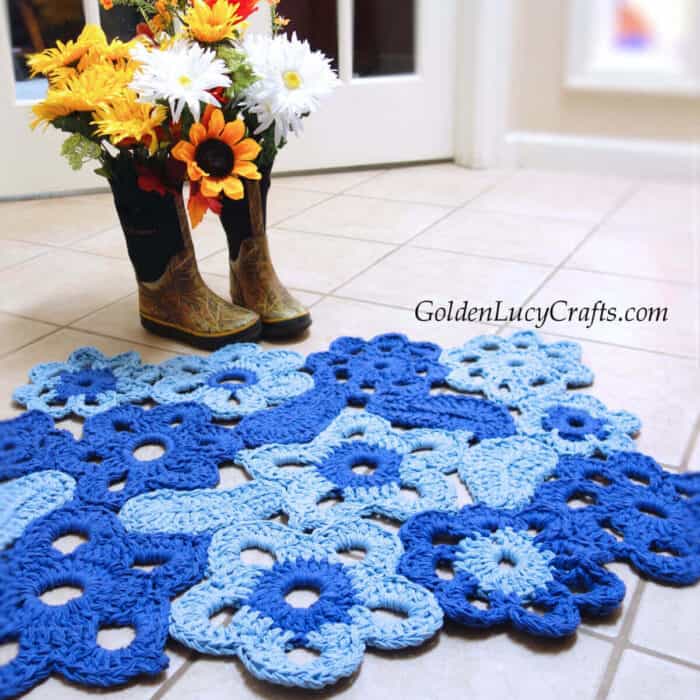 Crocheted flower rug on the floor, rainboots with flowers next to the rug.