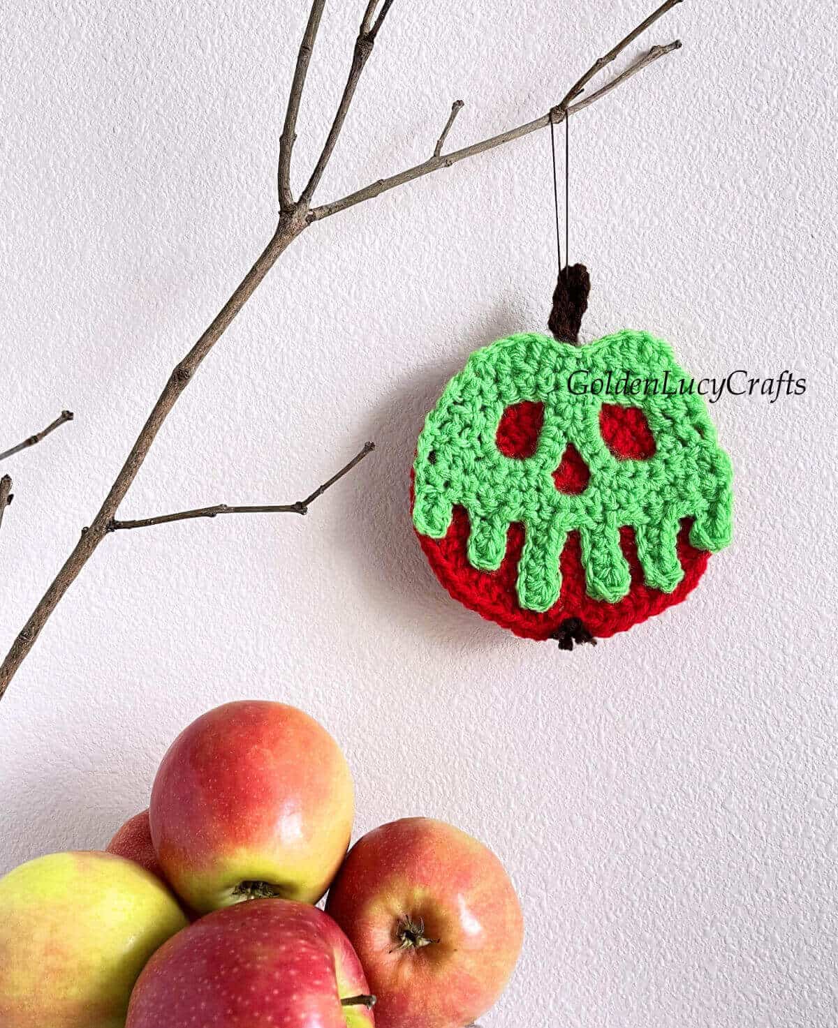 Crocheted poisoned apple ornament hanging on the branch.