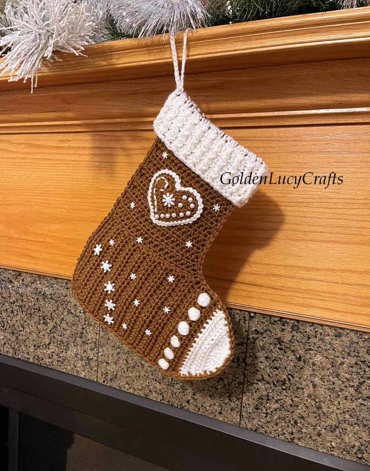 Crochet gingerbread Christmas stocking hanging on a fireplace.
