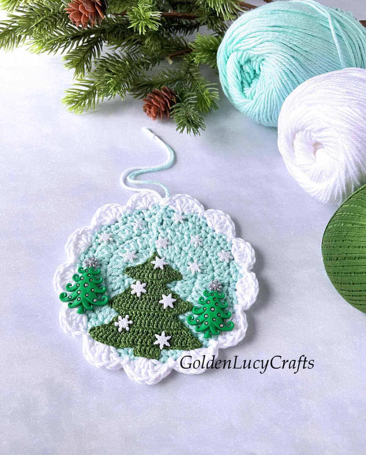 Crochet ornament with Christmas trees laying next to yarn skeins.