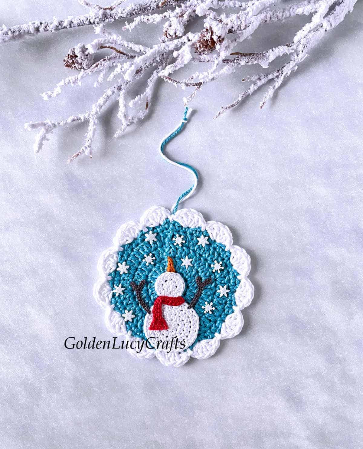 Crochet winter-themed ornament with snowman catching snowflakes on it.