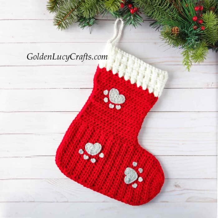 Crocheted red Christmas stocking embellished with paw print appliques.
