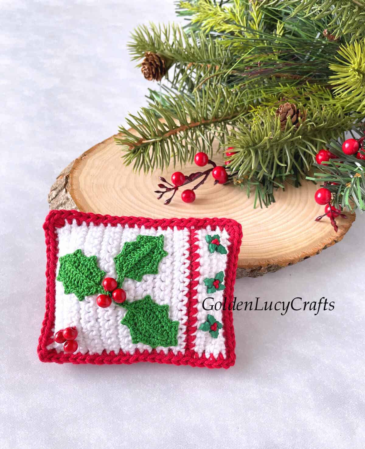 Crocheted Christmas mini pillow next to tree trunk slice and Christmas tree branch.