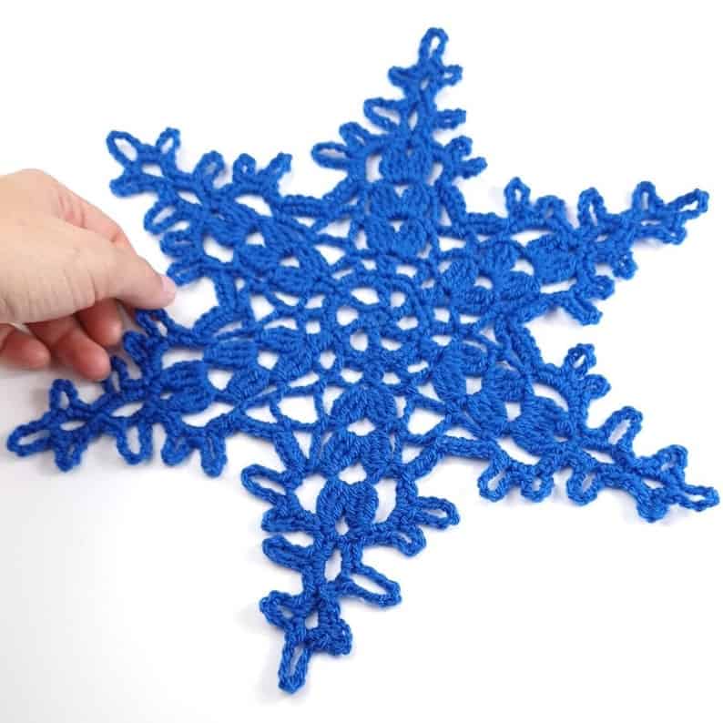 Crochet blue snowflake held by a hand.