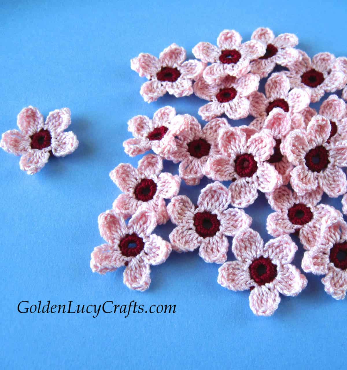 Crocheted pink cherry flowers on the blue background.