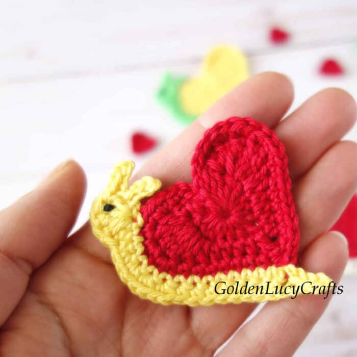 Crochet heart snail in the palm of a hand.