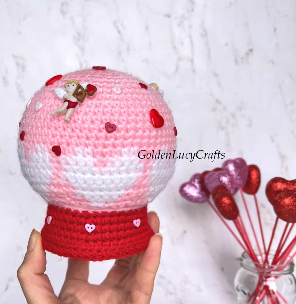Valentine's Day crochet snow globe held by a hand.