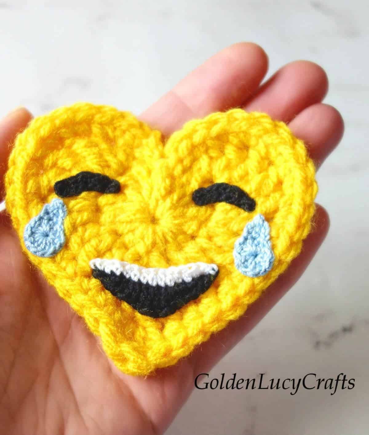 Crochet heart-shaped emoji in the palm of a hand.