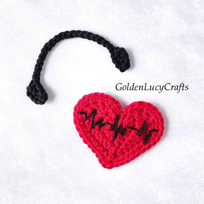 Crochet applique red heart with embroidered heartbeat and black headphones.