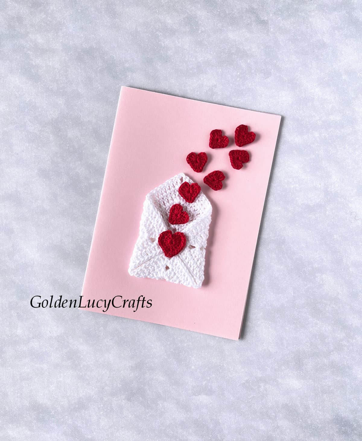 Pink card with crochet heart envelope and small red heart popping out of it.