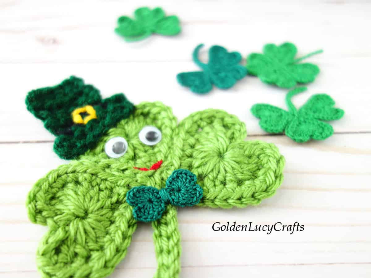 Crochet shamrock in a hat, with googly eyes and a bow.